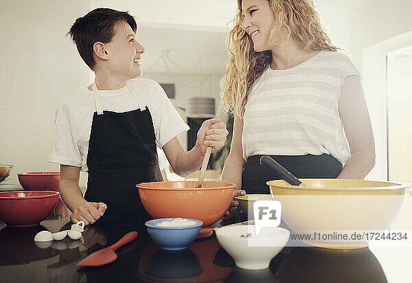 Lächelnde Mutter und Sohn schauen sich bei der Zubereitung von Speisen in der Küche zu Hause an
