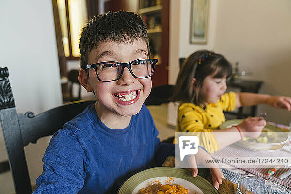 Junge lächelt mit Schwester beim Essen zu Hause