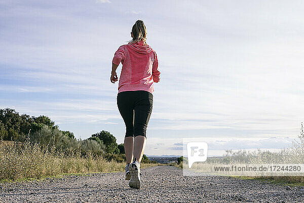 Female runner jogging on country road during sunny day