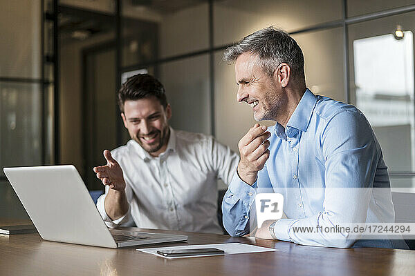 Smiling male professionals discussing over laptop in board room