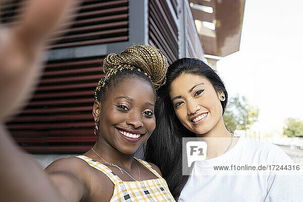 Woman with braided hair taking selfie with female friend outdoors