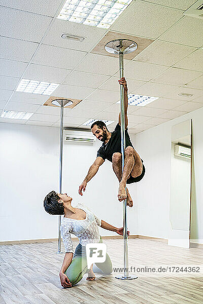 Tänzerin betrachtet männlichen Akrobaten beim Üben an der Stange im Tanzstudio
