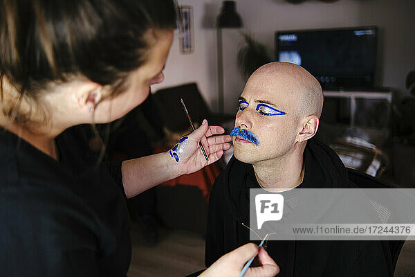 Female artist doing makeup of bald man in studio
