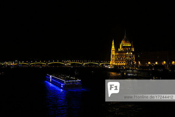 Beleuchtetes Passagierschiff mit dem Gebäude des ungarischen Parlaments in Budapest  Ungarn