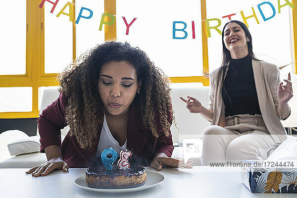Weibliche Fachkraft bläst Geburtstagskerze auf Kuchen während einer Feier im Coworking-Büro aus