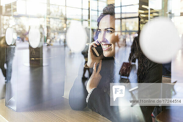 Lächelnde Geschäftsfrau  die wegschaut  während sie am Tisch mit ihrem Smartphone telefoniert