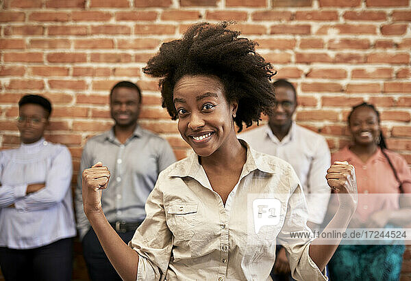 Lächelnde Geschäftsfrau  die Muskeln anspannt  mit männlichen und weiblichen Mitarbeitern im Hintergrund im Büro