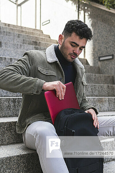 Businessman putting laptop inside backpack while sitting on steps