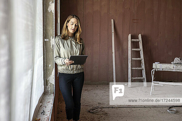 Weibliche Fachkraft  die ein digitales Tablet benutzt  während sie sich an der Wand in der Nähe des Fensters anlehnt