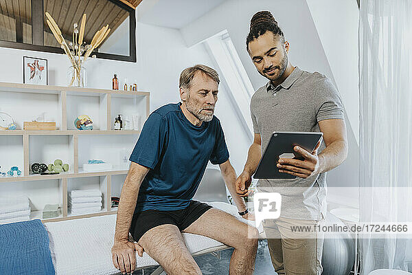 Male physiotherapist showing digital tablet to patient in practice