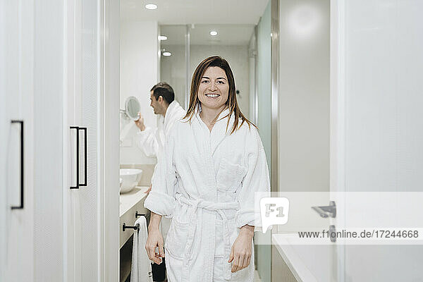 Smiling woman wearing bathrobe standing in hotel bathroom