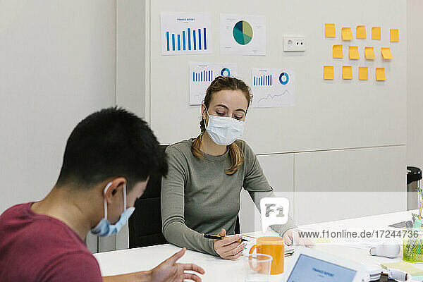 Männliche und weibliche Fachkraft mit Schutzmaske bei der Arbeit am Schreibtisch in einem Coworking-Büro während einer Pandemie