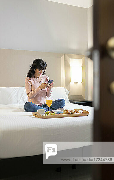 Reife Frau  die ein Mobiltelefon benutzt  sitzt auf dem Bett einer Hotelsuite
