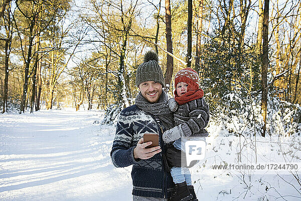 Father with smart phone carrying son on snow during winter