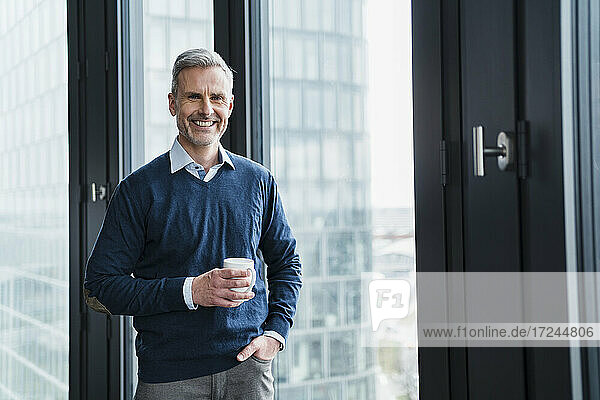 Male professional with coffee cup standing by window in office