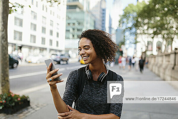 Lächelnde junge Frau  die in der Stadt auf ihr Mobiltelefon schaut