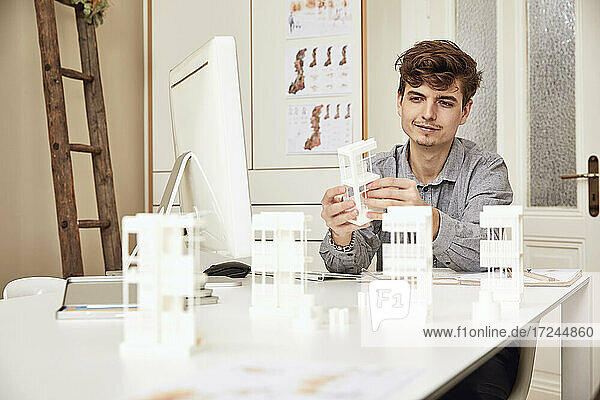 Male architect examining architectural model while sitting at table