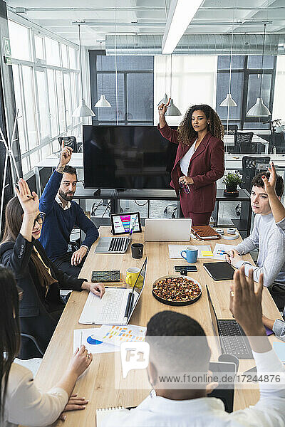 Male and female entrepreneurs raising hands during meeting in office