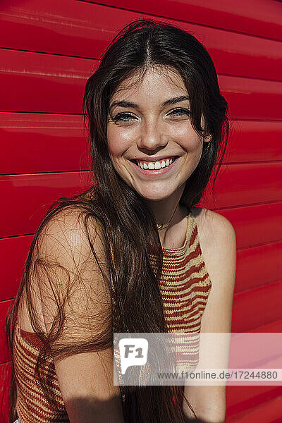 Lächelnder weiblicher Teenager vor einer roten Wand stehend