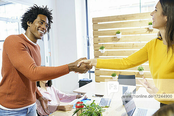 Lächelnde kreative Geschäftsleute  die sich im Büro die Hände schütteln
