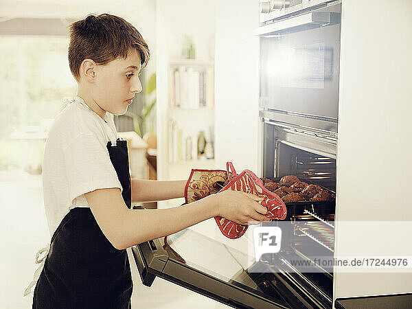 Junge nimmt Muffinblech aus dem Ofen in der Küche zu Hause