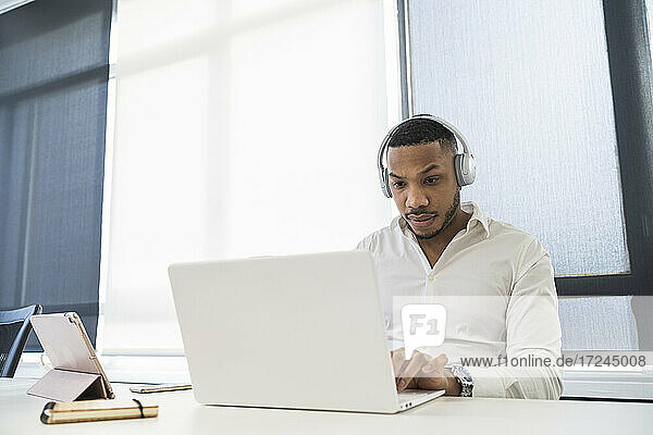 Männlicher Unternehmer mit Kopfhörern bei der Arbeit am Laptop im Büro