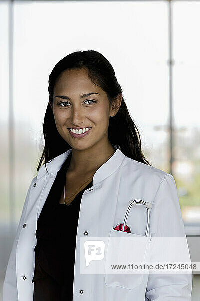 Lächelnde Frau im Laborkittel vor einem Krankenhausfenster