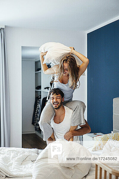 Cheerful young woman having pillow fight with boyfriend in bedroom