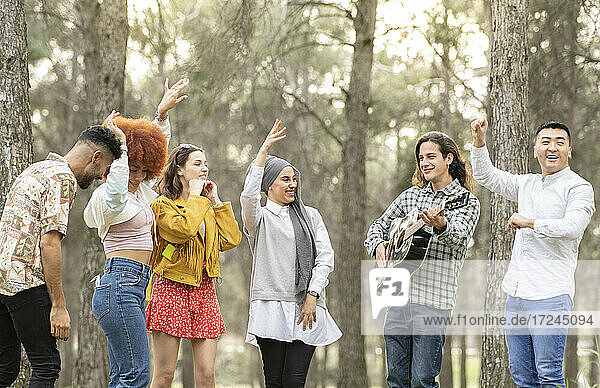 Fröhliche multiethnische weibliche und männliche Freunde tanzen und vergnügen sich im Wald