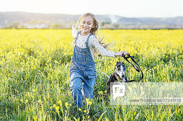 Lächelndes Mädchen läuft mit Hund in einem landwirtschaftlichen Feld