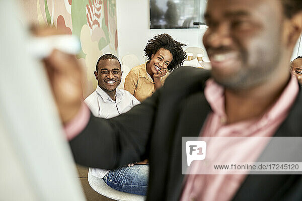 Lächelnde männliche Fachkraft  die mit Kollegen im Büro eine Geschäftsstrategie am weißen Brett diskutiert