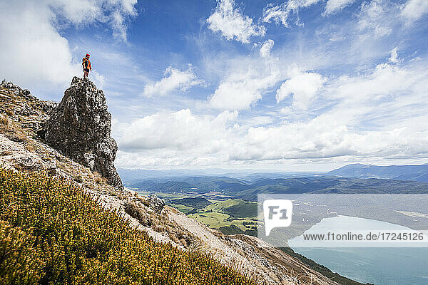 New Zealand  Tasman District  Male hiker standing on top of rock formation overlooking scenic Lake Rotoiti