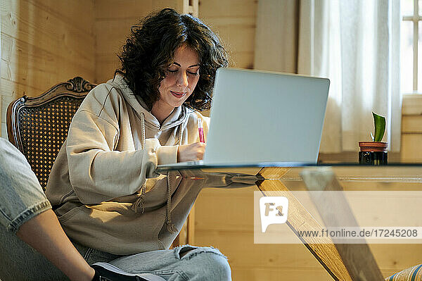 Mittlere erwachsene Frau beim Schreiben vor einem Laptop bei der Arbeit zu Hause