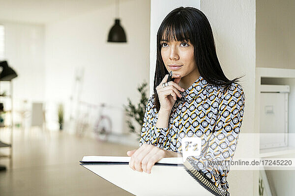 Nachdenkliche Geschäftsfrau mit Notizbuch an einer Säule im Büro