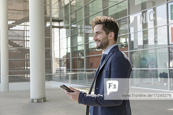 Businessman holding smart phone while looking away
