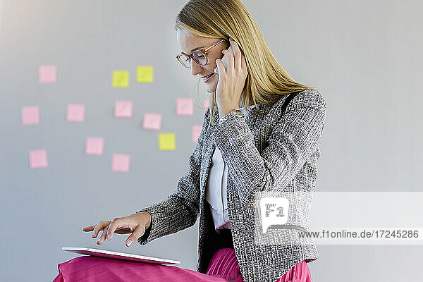 Unternehmerin  die mit einem Smartphone spricht  während sie im Büro ein digitales Tablet benutzt