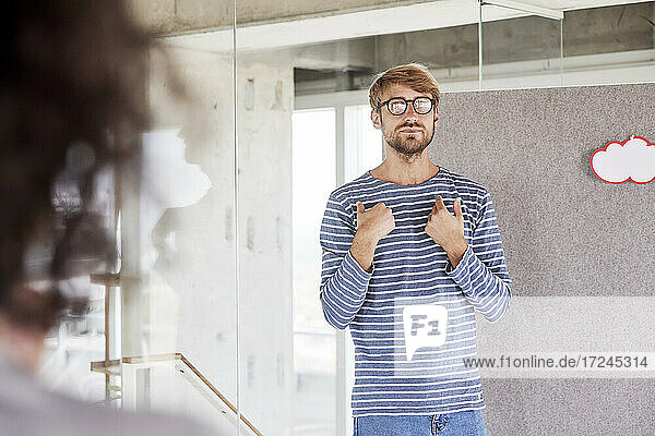 Handsome man wearing eyeglasses gesturing while standing in front of partition wall