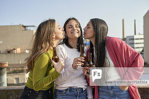 Weibliche Freunde küssen junge Frau beim Biertrinken auf dem Dach