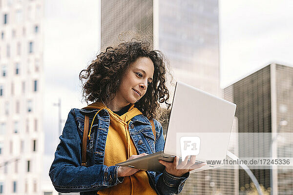 Frau in Jeansjacke mit Laptop in der Stadt