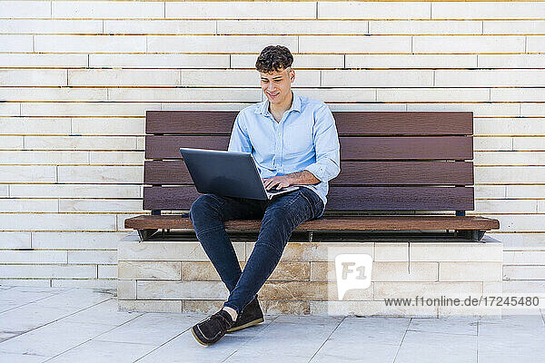 Geschäftsmann  der einen Laptop benutzt und auf einer Bank sitzt
