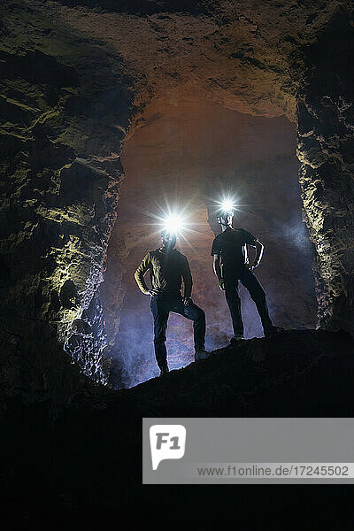 Male tourists exploring cave wearing illuminated headlamps