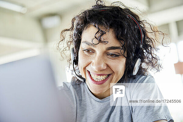 Cheerful woman wearing headphones looking at laptop