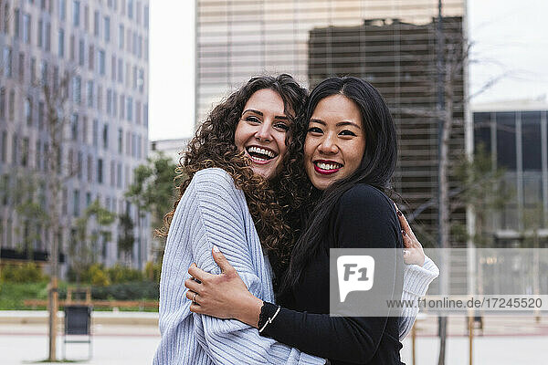 Happy woman looking away while embracing friend in city