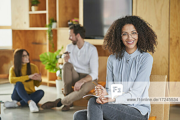 Mid adult businesswoman smiling while sitting with colleagues in background