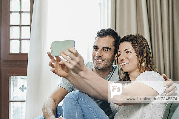 Lächelndes mittleres erwachsenes Paar  das ein Selfie mit dem Handy macht  während es im Hotelzimmer sitzt