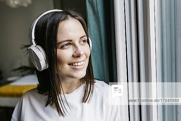 Lächelnde Frau mit In-Ear-Kopfhörern träumt zu Hause vor sich hin