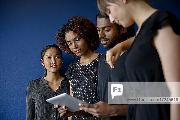 Geschäftsfrau mit Blick auf internationale männliche und weibliche Kollegen  die an einem digitalen Tablet vor blauem Hintergrund arbeiten