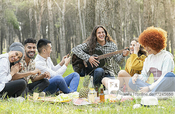 Mann mit männlichen und weiblichen Freunden spielt Gitarre beim Picknick im Wald