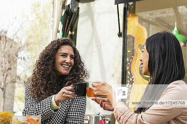 Lächelnde Frauen stoßen mit einem Getränk in einem Straßencafé an