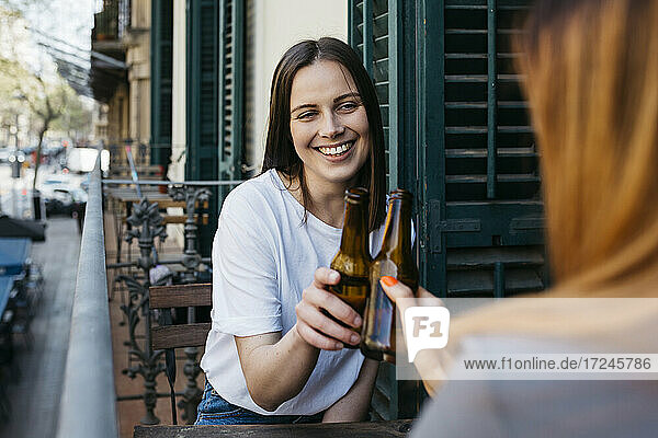 Junge Frauen stoßen mit Bierflaschen an  während sie auf dem Balkon sitzen